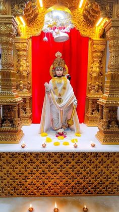 an idol is sitting in front of a red curtain with gold decorations on the floor