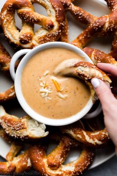 a person dipping something into a bowl with pretzels in the background on a plate