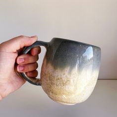 a hand holding a gray and white coffee mug