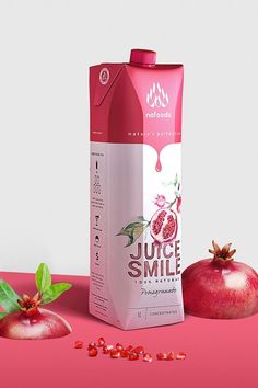 a carton of juice sitting next to two pomegranates on a pink surface