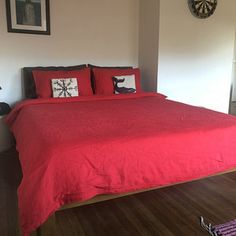 a bed with red sheets and pillows in a bedroom next to a wall mounted clock