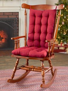 a wooden rocking chair with red cushions in front of a christmas tree and fire place