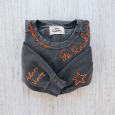 a gray shirt with orange writing on it sitting on a white wooden surface and hanging from the wall