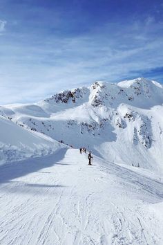 people are skiing on the snow covered mountain side with mountains in the backgroud