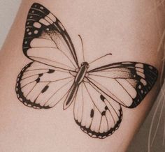 a black and white butterfly tattoo on the right side of the arm, with dots all over it's wings