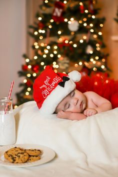 a baby in a santa hat laying on a bed next to cookies