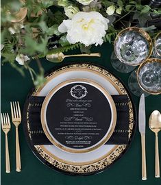 a table setting with gold and black plates, silverware, and flowers on it