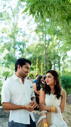 a man and woman standing next to each other in front of some trees with people looking on