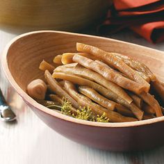 a wooden bowl filled with sliced up carrots on top of a table next to a knife