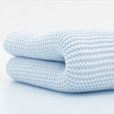 two blue knitted blankets folded on top of each other in front of a white wall