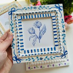 a hand holding a blue and white frame with flowers on it