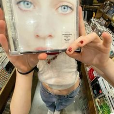 a woman holding up a cd in front of her face with blue eyes and red nail polish