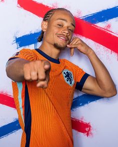 a young man pointing at the camera with his hand on his hip and wearing an orange shirt