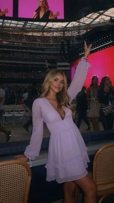 a woman posing for the camera in a purple dress at a sporting event with her hand up