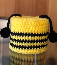 a crocheted yellow and black hat sitting on top of a glass table