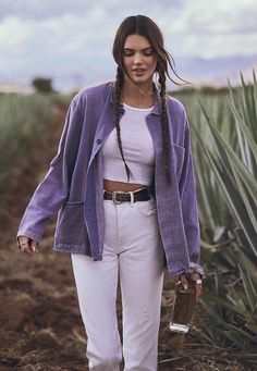 a woman walking down a dirt road next to a field