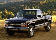 a black pickup truck parked on top of a dirt road in front of trees and mountains