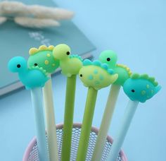 four green and blue dinosaur shaped pens in a cup