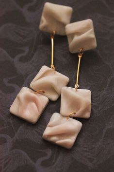 three square shaped white and gold earrings on a black surface