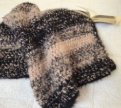 two black and white knitted mittens sitting on top of a bed next to an open book