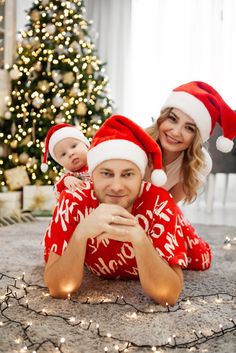 a man and woman are laying on the floor with their baby wearing christmas pajamas, hats and stockings