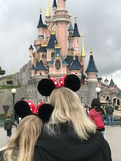 two people wearing minnie mouse ears in front of a castle