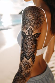 a woman with a turtle tattoo on her arm and shoulder, standing next to the ocean