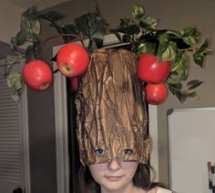 a woman wearing a paper bag over her head with apples hanging from it's sides