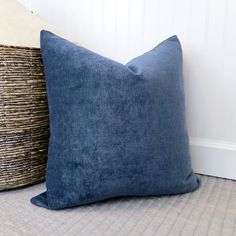 two blue pillows sitting next to each other on top of a carpeted floor in front of a white wall