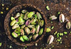 a wooden bowl filled with green sprouts on top of a stone floor next to nuts