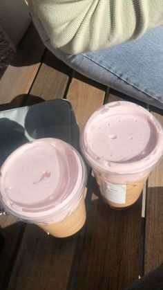 two plastic cups sitting on top of a wooden table next to a person's leg