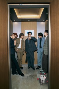 four young men in suits are looking at something on the ground while standing in an elevator