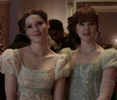 two women in gowns standing next to each other with candles on the table behind them