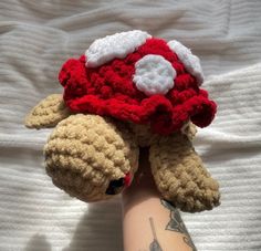 a person's arm with a stuffed animal wearing a red and white crochet hat