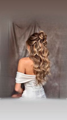 a woman with long curly hair in a white dress is looking at the back of her head