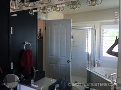 a woman taking a selfie in a bathroom mirror with lights hanging from the ceiling