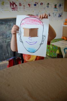 a young boy holding up a paper cut out of his face