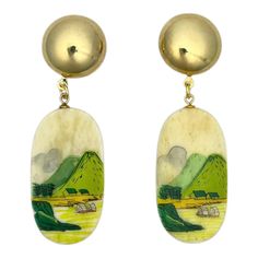 two gold toned earrings with mountains and clouds in the background, one has green grass on it