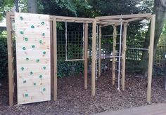 an outdoor play area with climbing bars and wooden structures on the ground, surrounded by trees