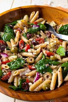 a wooden bowl filled with pasta salad on top of a table