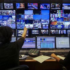 two people sitting at a desk in front of multiple monitors