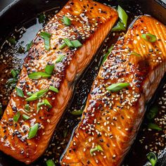 two salmon fillets in a skillet with sesame seeds and seasoning on top