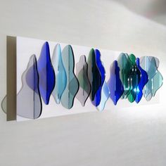 a group of blue and green glass pieces hanging on a white wall next to each other