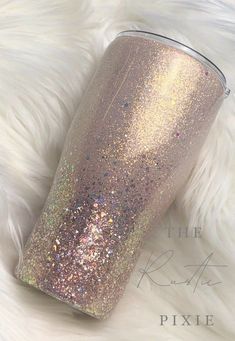 thermos cup is sitting on top of a white fur covered surface with gold and silver flecks