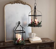 two candles are lit on a table next to a mirror and vase with greenery