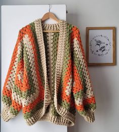 an orange and green crocheted sweater hanging on a wall next to a framed photograph