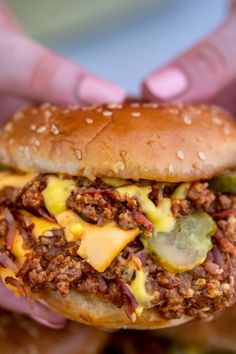 a person holding up a cheeseburger in their hands