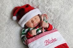 a baby wearing a santa hat and holding a candy cane while laying on a white blanket