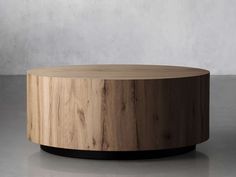 a round wooden table sitting on top of a cement floor next to a white wall