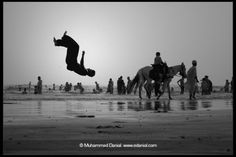 a person jumping in the air on top of a horse near some people and water